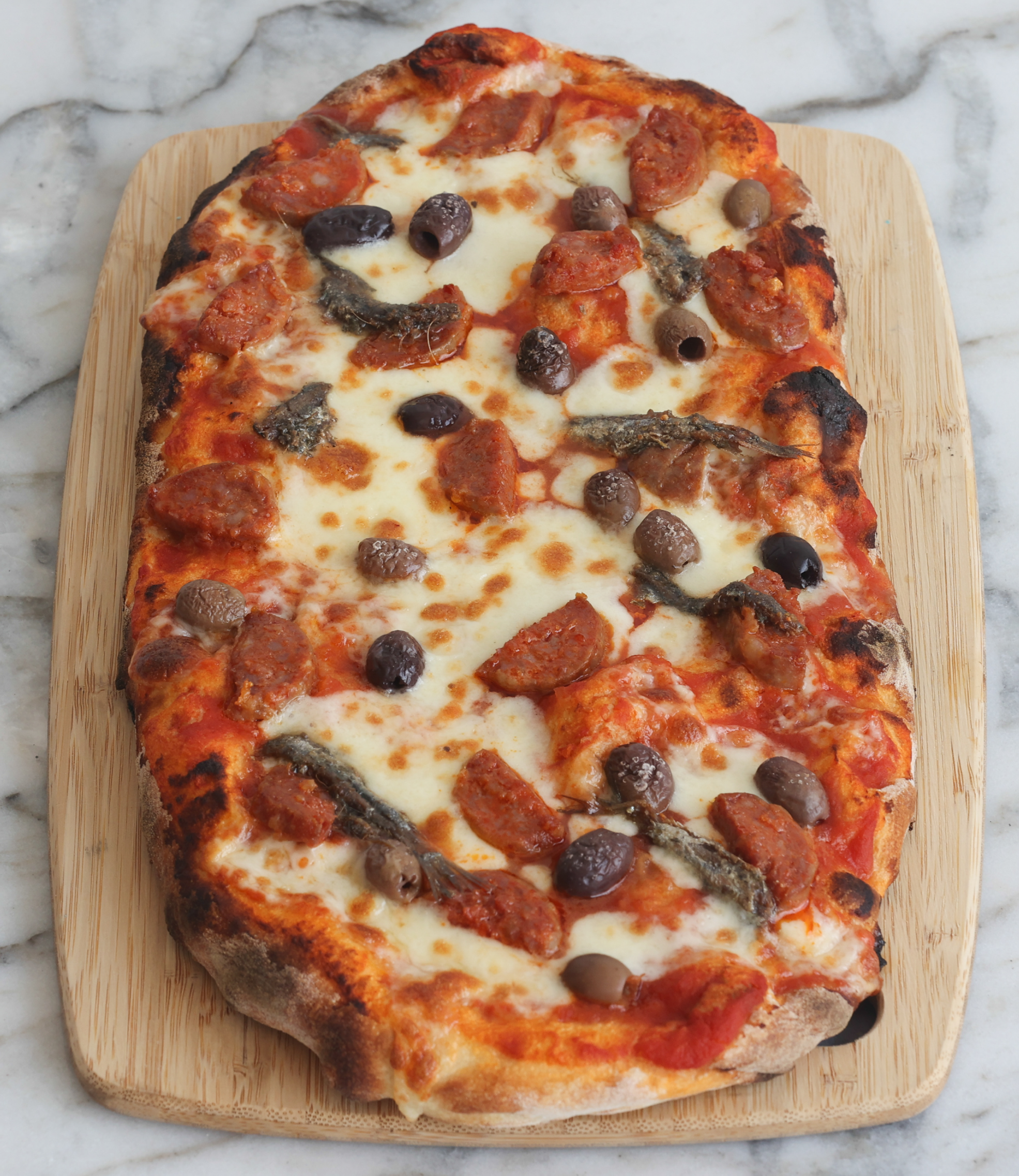 Calabrese pinsa with mozzarella, olives, anchovy, and spicy salami